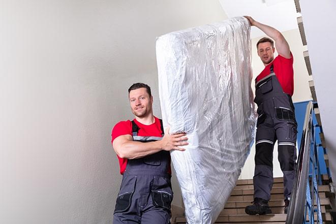 two people carrying a box spring out of a bedroom in Bensenville